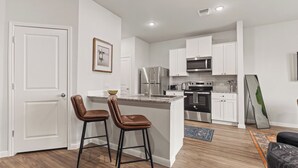 A modern kitchen with white cabinets, stainless steel appliances, and a central island with two bar stools.