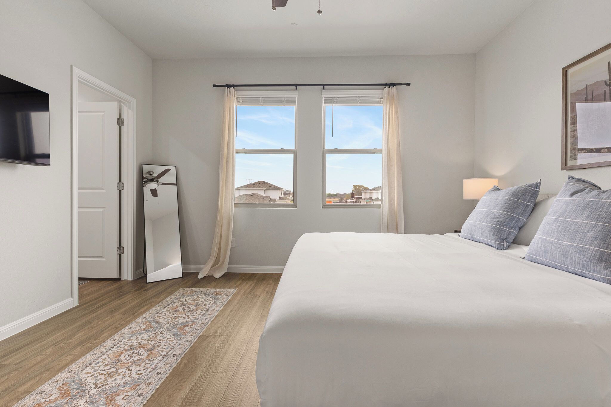 A bedroom with a bed, a window with curtains, a door, and a mounted TV.