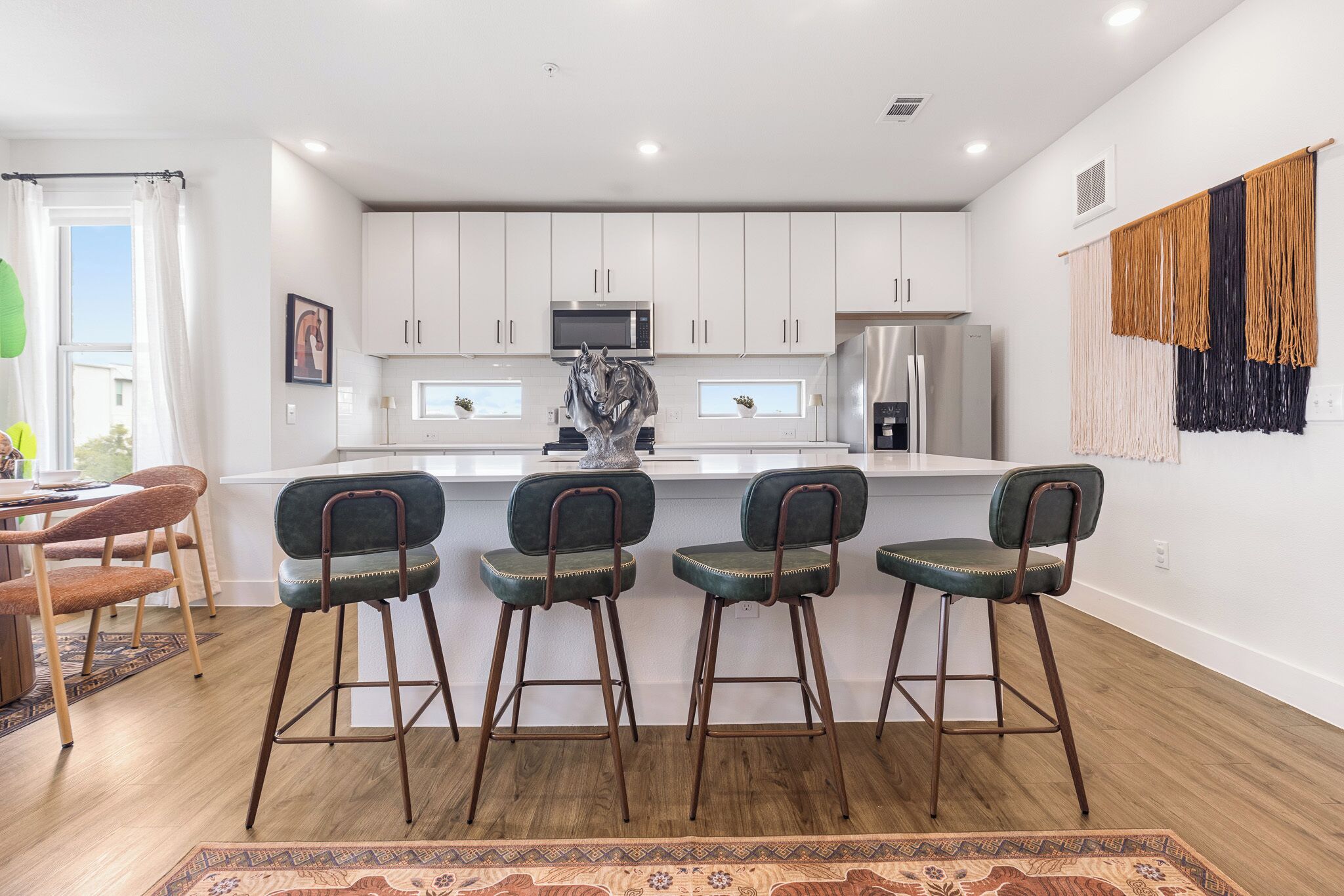 A modern kitchen with white cabinets, a central island with bar stools, and a decorative horse sculpture.