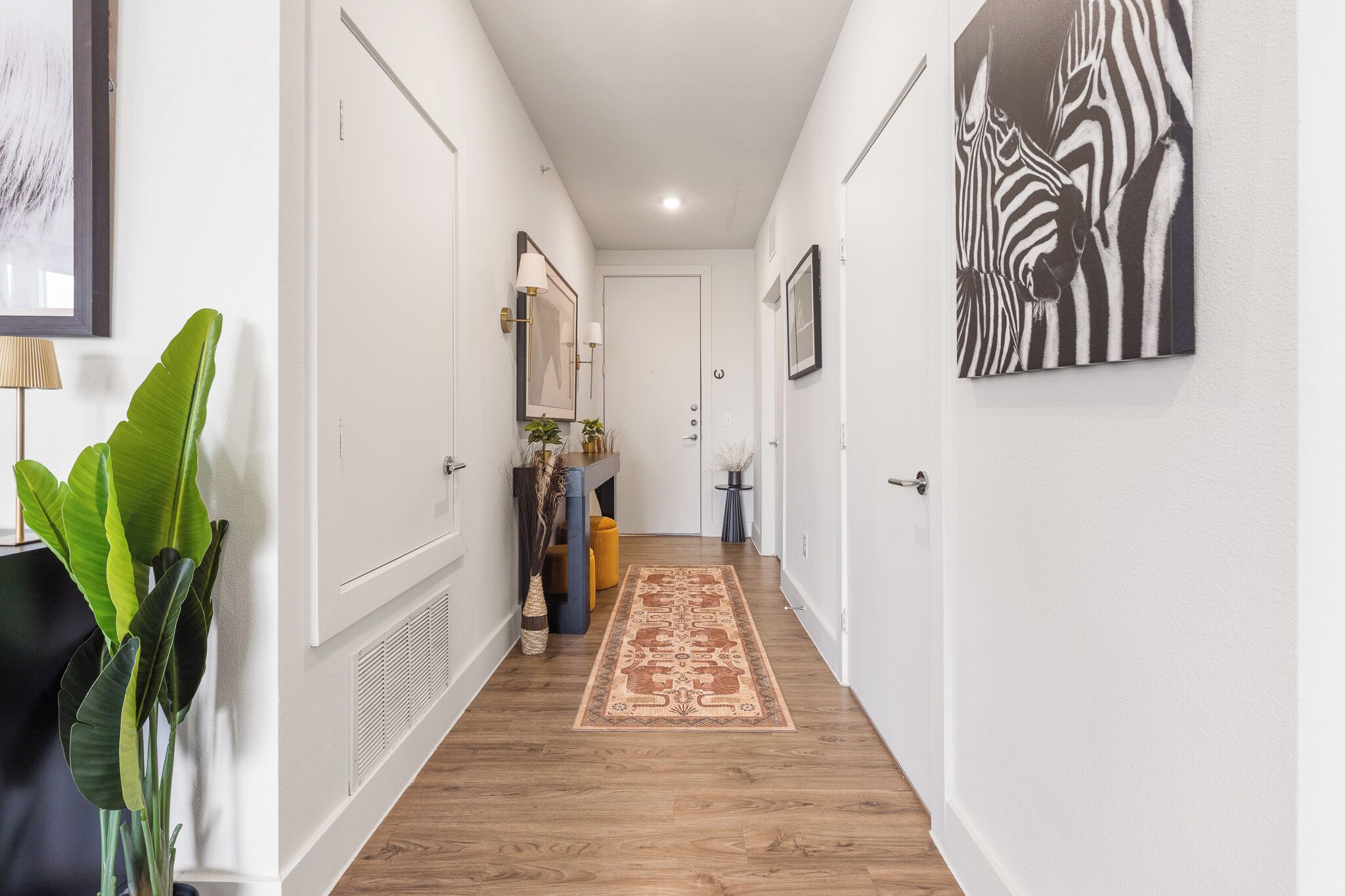 Un pasillo con paredes blancas, piso de madera, alfombra estampada y un cuadro de cebra en la pared.