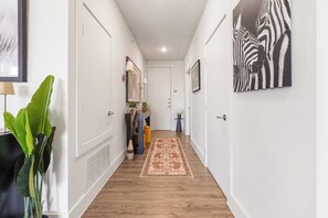 A hallway with white walls, a wooden floor, a patterned rug, and a zebra artwork on the wall.