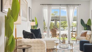 En moderne stue med sofa, sofabord og stole, store vinduer med gardiner og indeplanter.