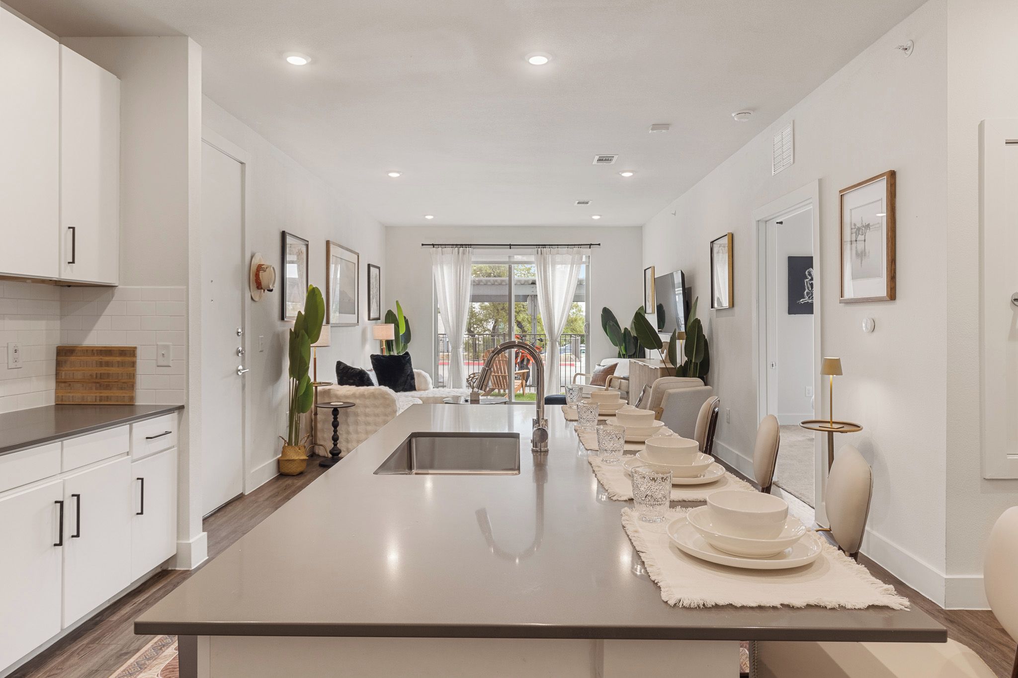 Una cocina moderna con una isla central, muebles blancos y una zona de comedor con una mesa larga preparada para cuatro personas.
