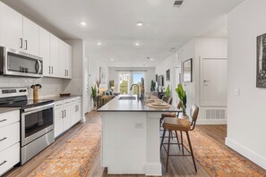 A modern kitchen with white cabinets, stainless steel appliances, and a central island with bar stools. - Modern 1BR Retreat w/ Resort Pool& Stylish Living (Austin)