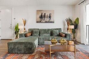 A living room with a sectional sofa, a coffee table, and a painting of horses. - Modern 1BR Retreat w/ Resort Pool& Stylish Living (Austin)