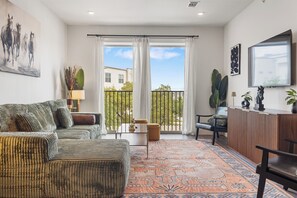 A spacious living area with a sofa, a coffee table, a patterned rug, a balcony with a view, and a wooden sideboard. - Modern 1BR Retreat w/ Resort Pool& Stylish Living (Austin)