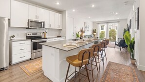 Une cuisine moderne avec des meubles blancs, des appareils en acier inoxydable et un îlot central doté de tabourets de bar.