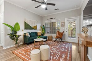 Un salon avec un canapé vert, un ventilateur de plafond, une grande plante et un tapis à motifs.