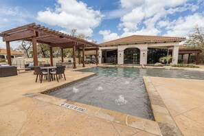 Un espace piscine agrémenté d’une pergola, de sièges d’extérieur et d’un bâtiment doté d’un toit en tuiles.