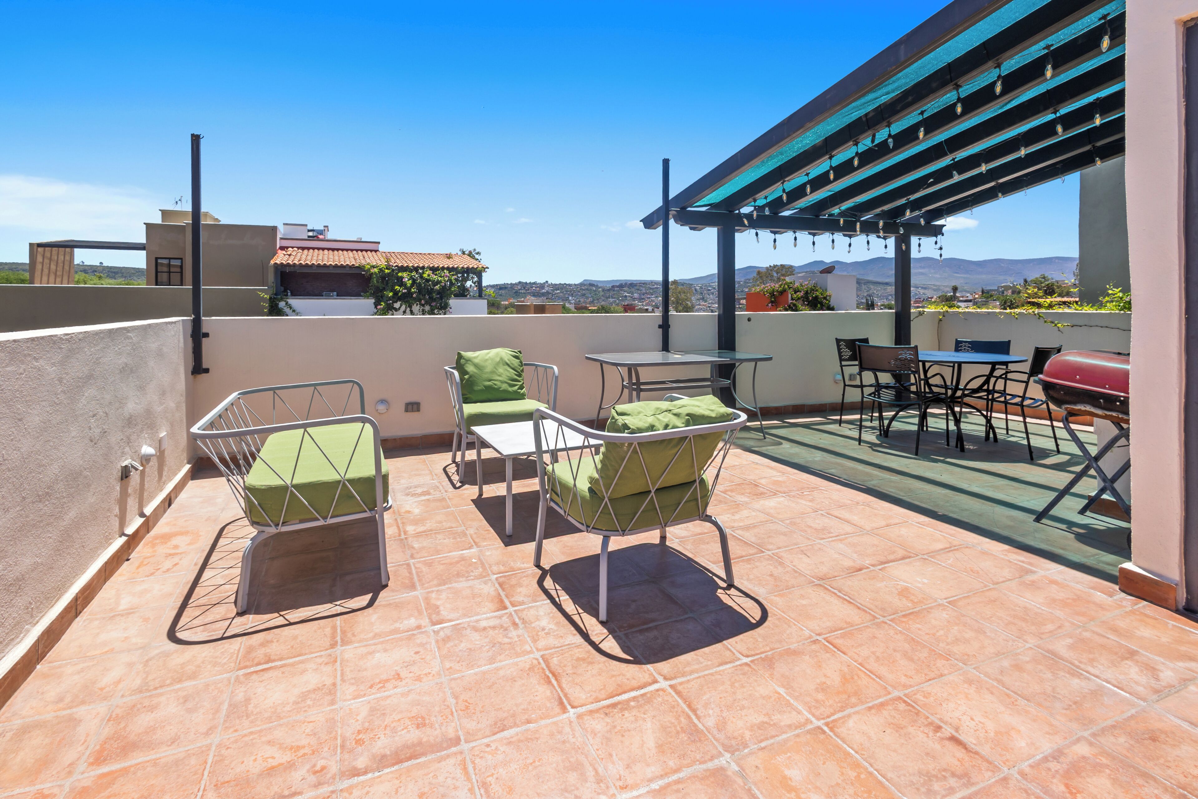 A rooftop terrace with outdoor seating, a barbecue grill, and a pergola with string lights.