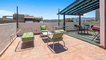 A rooftop terrace with outdoor seating, a barbecue grill, and a pergola with string lights.