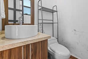 Une salle de bain avec un lavabo blanc, un meuble-lavabo en bois, un porte-serviettes en métal et des toilettes blanches.