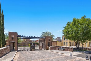 Une entrée fermée par un portail, agrémentée d’une pergola, de murs en pierre, d’un banc et d’un arbre.