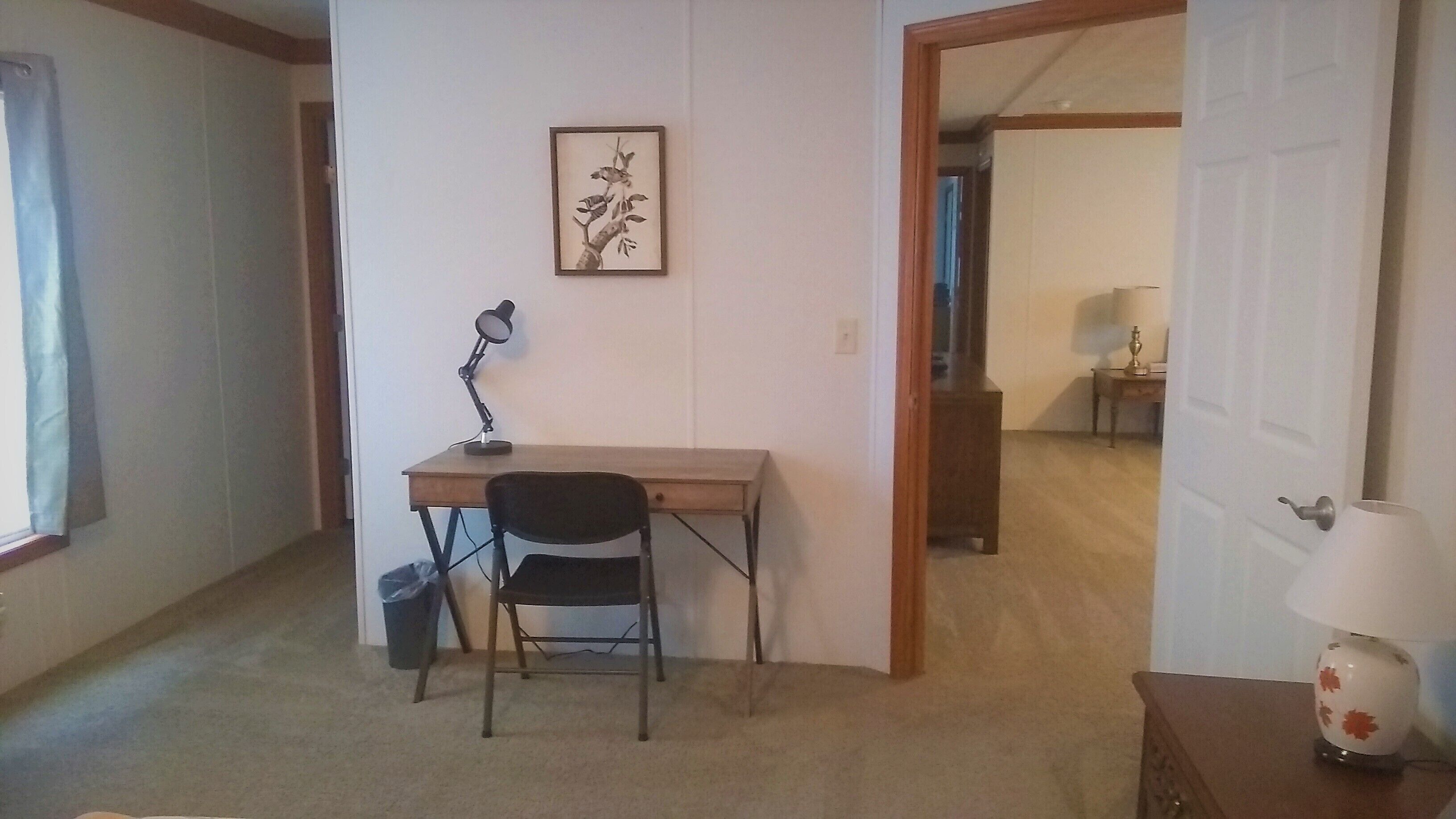 Une petite pièce, peu meublée, avec un bureau, une chaise et un tableau encadré accroché au mur.
