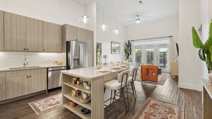 A modern kitchen with wooden cabinets, stainless steel appliances, and a central island with bar stools. - Spacious 1BR w/ Patio, Pool & Gym Access (Austin)