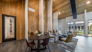 A modern interior with a wooden ceiling, large windows, a dining area with round tables and chairs, and a visible outdoor pool. - Spacious 1BR w/ Patio, Pool & Gym Access (Austin)
