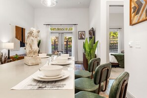 Ein Essbereich mit einem langen Tisch, der für sechs Personen gedeckt ist, Stühlen, einer dekorativen Tischmitte und Blick durch eine Glastür nach draußen.