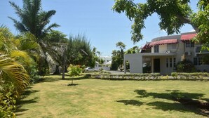 A well-maintained lawn with palm trees, a building with a red awning, and a clear blue sky. - Tamarind Tree Hotel (Runaway Bay)