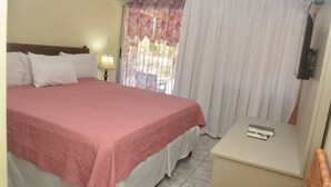 A hotel room with a bed, a bedside table, a lamp, and a window with curtains. - Tamarind Tree Hotel (Runaway Bay)