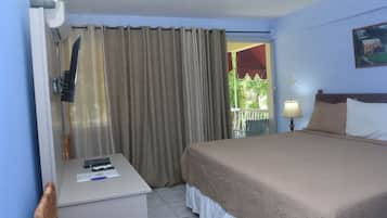 A hotel room with a bed, a desk with a lamp, a window with curtains, and a painting on the wall.