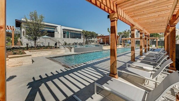Ein Poolbereich mit Liegestühlen, einer Pergola und einem modernen Gebäude im Hintergrund.