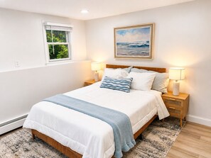 A bedroom with a bed, two bedside tables with lamps, a window, and a painting on the wall.
