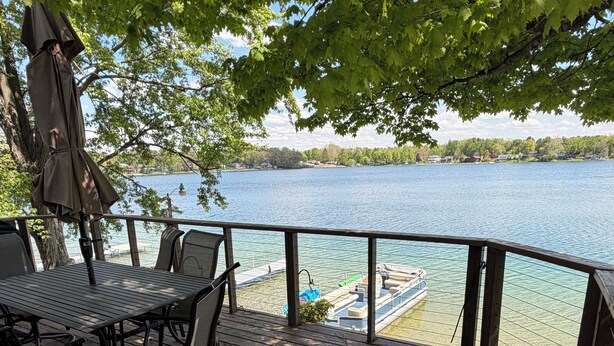 Una terraza de madera con mobiliario exterior, vista a un lago y un muelle con un bote.