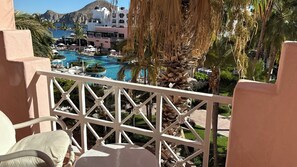 Un balcó amb vista a una piscina, palmeres i un edifici de façana blanca.