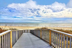 A wooden boardwalk leading to a beach with a clear sky.
