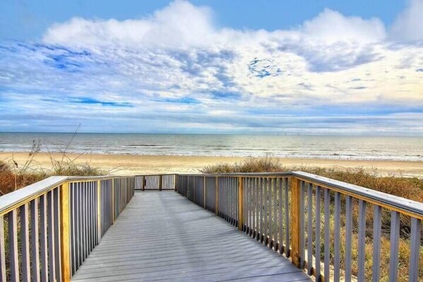 A wooden boardwalk leading to a beach with a clear sky.
