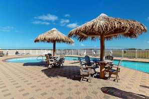 A poolside area with thatched umbrellas, lounge chairs, and a view of the ocean.