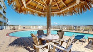 Un espace aménagé au bord de la piscine, avec un parasol en chaume, des chaises en bois et une piscine.