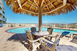 A poolside area with a thatched umbrella, wooden chairs, and a pool.