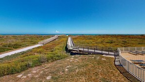 Une promenade en bord de mer, avec une allée en bois et des bancs, entourée d’une végétation naturelle.