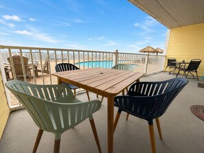 Uma varanda com mesa e cadeiras de madeira, piscina e um guarda-sol de palha.