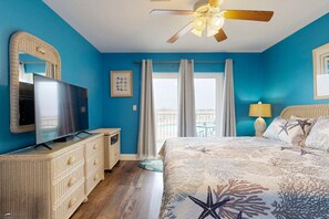 Quarto com cama, televisão, cômoda, ventoinha no teto e vista para a varanda.