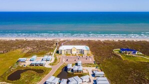 Vue aérienne d’un hôtel situé sur la côte, composé de plusieurs bâtiments, d’un parking et d’une plage.