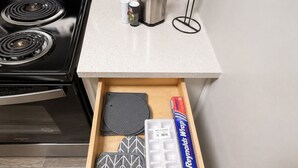 A kitchen drawer with a stainless steel stove, a white countertop, and various kitchen items including a box of Reynolds Wrap. - Olive & Elm Hoover | Cozy Modern Escape *1Bed* (Hoover)