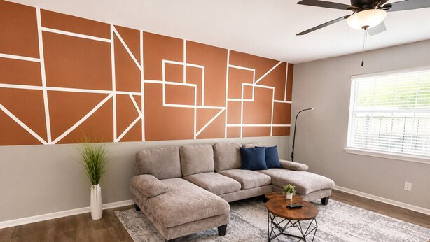A living room with a sectional sofa, a coffee table, a potted plant, and a geometric wall design. - Olive & Elm Hoover | Cozy Modern Escape *1Bed* (Hoover)