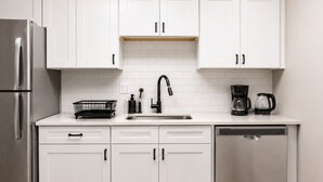 A modern kitchen with white cabinets, a stainless steel refrigerator, a dishwasher, and a coffee maker. - Olive & Elm Hoover | Cozy Modern Escape *1Bed* (Hoover)