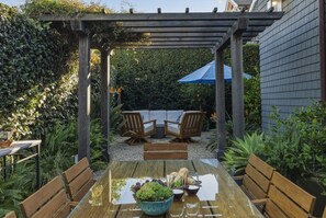 Eine Holzpergola mit Tisch und Stühlen, umgeben von viel Grün.