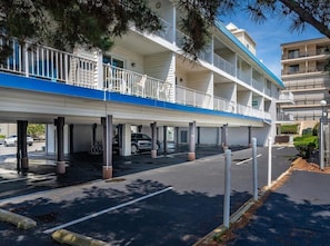 Ein mehrstöckiges Hotel mit überdachtem Parkbereich, Balkonen und blauem Himmel.