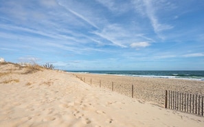 Une plage avec un sentier de sable, une clôture en bois et l’océan en arrière-plan.