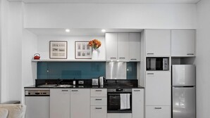 Uma cozinha moderna com armários brancos, bancada preta, chaleira vermelha, micro-ondas e geladeira.