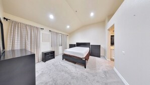 A bedroom with a bed, a dresser, a nightstand, a closet, and a bathroom visible through an open door. -     Fully Furnished Anaheim Townhome - Utilities Included - Gated Community (Anaheim)