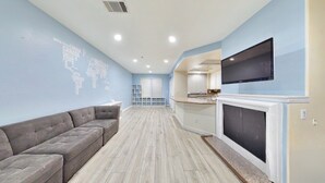 A living room with a grey sofa, a flat-screen TV mounted above a fireplace, and a world map on the wall. -     Fully Furnished Anaheim Townhome - Utilities Included - Gated Community (Anaheim)