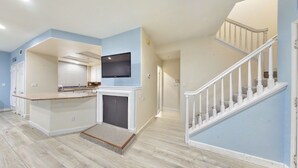 A spacious living area with a kitchen, a fireplace, a TV mounted above it, and a staircase leading to another level. -     Fully Furnished Anaheim Townhome - Utilities Included - Gated Community (Anaheim)