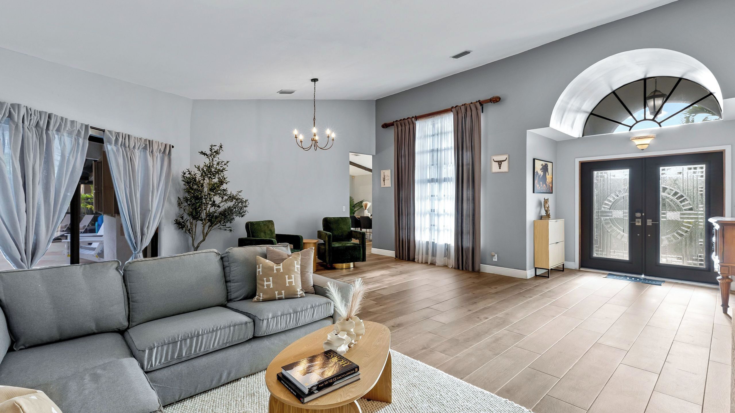 A modern living room with a grey sofa, a wooden coffee table, and a chandelier.