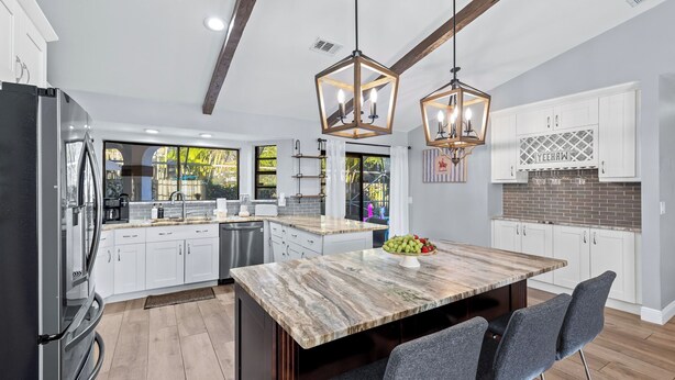 A modern kitchen with a marble island, pendant lights, and a view to the outside.