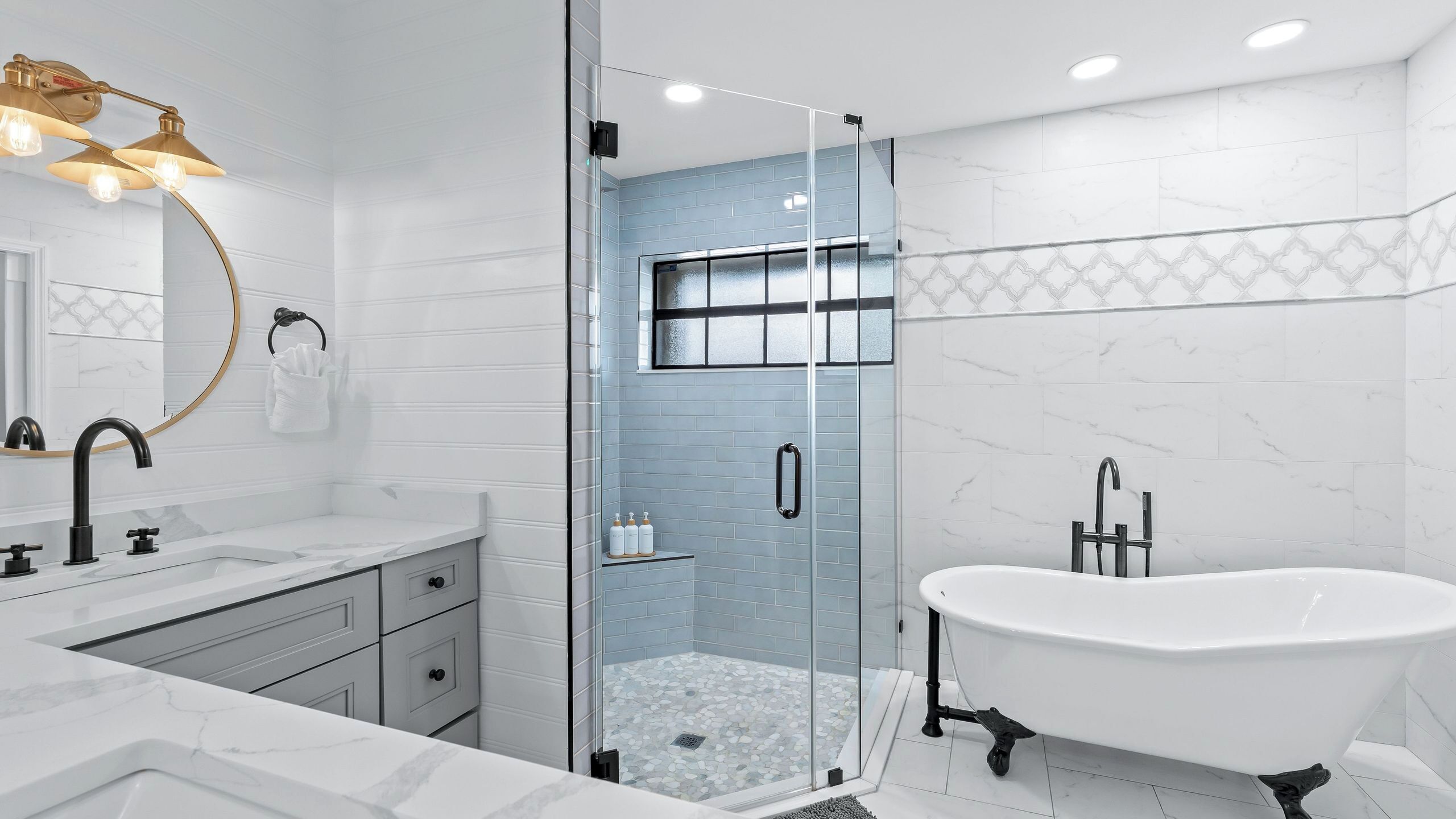 A modern bathroom with a freestanding bathtub, a glass-enclosed shower, and a vanity with a mirror and light fixture.